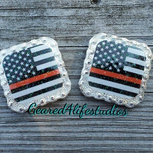 May include: Two silver-toned square-shaped belt buckles with a glittery American flag design and a thin red stripe across the middle. The text "Geared4lifestudios" is visible below the buckles.