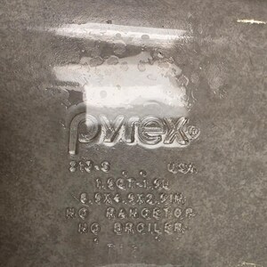 Puede incluir: Una fuente de horno de vidrio transparente con texto en relieve Pyrex, 1.5QT-1.4L, 8.5x4.5x2.5IN, NO RANGETOP, NO BROILER. El recipiente rectangular presenta letras moldeadas en la base que indican la capacidad, dimensiones y advertencias.