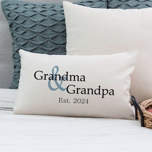 May include: White throw pillow with the text "Grandma & Grandpa Est. 2024" in black lettering and a blue ampersand.