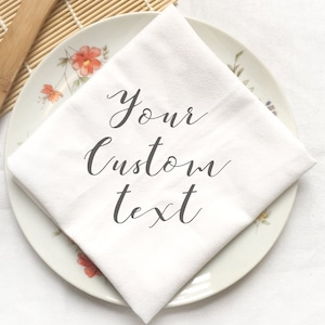 May include: White napkin with the text "Your custom text" on a white plate with a floral design. Two wooden spoons are in the background.