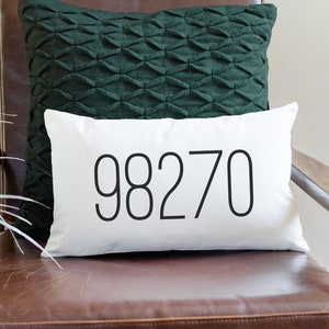 May include: A white lumbar pillow with the number 98270 printed in black on the front. The pillow is sitting on a brown leather armchair with a dark green pillow behind it.