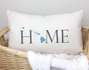 Puede incluir: Almohada blanca con la palabra "HOME" en texto gris y el estado de Hawái en azul, delineado en gris.