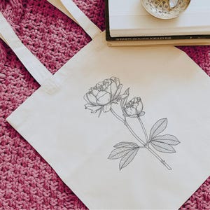 May include: A white tote bag with a black line drawing of a peony flower with two blooms and leaves.