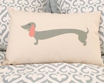 May include: A white pillow with a gray dachshund silhouette printed on it. The dachshund is smiling and has a pink tongue.