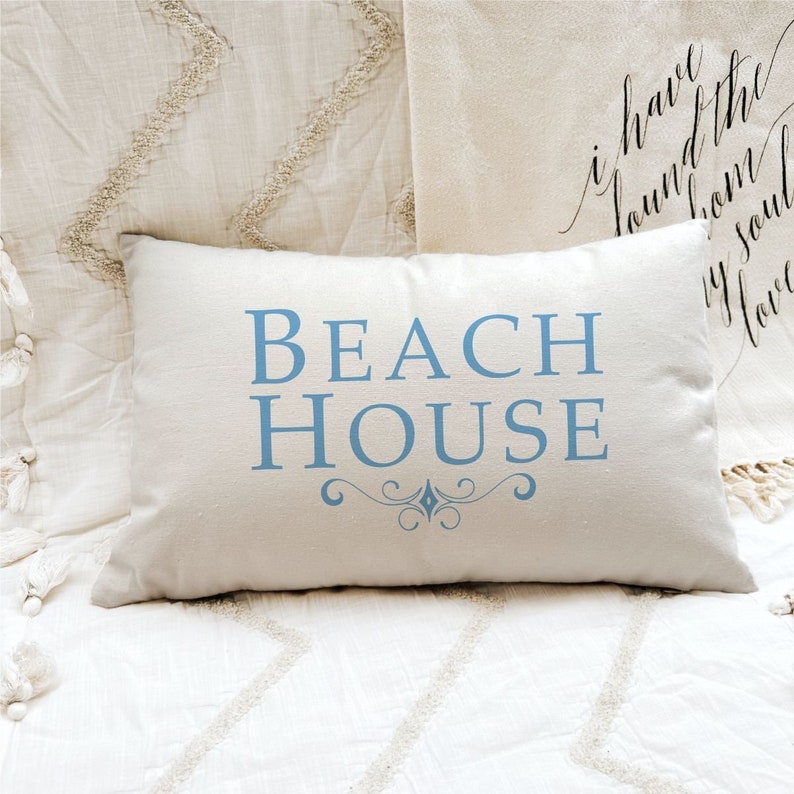 May include: A white pillow with the text "BEACH HOUSE" in blue lettering. The pillow has a decorative blue swirl design below the text.