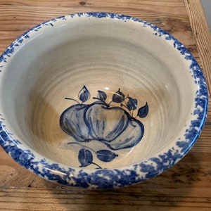 Könnte beinhalten: Eine cremefarbene Keramikschüssel mit blauem Blumendesign. Die Schüssel hat einen blau gesprenkelten Rand und ein handgemaltes blaues Kürbis- und Blättermotiv in der Mitte. Die Schüssel wird wahrscheinlich zum Servieren oder Ausstellen verwendet.