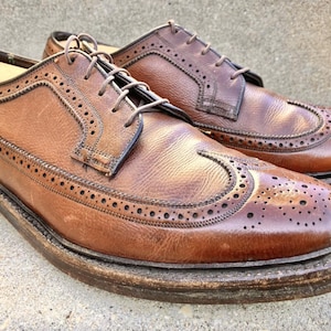 May include: A pair of brown leather brogue shoes with decorative perforations and a classic lace-up design. The shoes have a worn, textured appearance, suggesting they are vintage or well-loved. The soles are thick and show signs of wear.