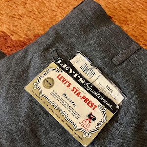 May include: Close-up of gray Levi's Sta-Prest trousers with original tags. The tags read "Levi's Sportswear" and "Never Needs Ironing." The trousers are made of a blend of Nylox, Zantrel, and Acetate.