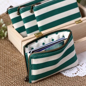 May include: A rectangular zippered pouch featuring a dark green and white horizontal striped pattern on the exterior. The interior lining is white with a green polka dot print. The pouch contains several rectangular cards inside the main compartment.