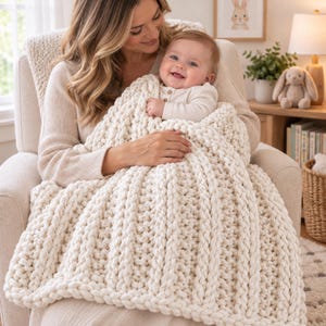 May include: A chunky knit blanket in a cream color featuring a thick, vertical ribbed texture. The blanket is crafted from soft, heavy yarn with a prominent braided stitch pattern that creates a cozy, tactile surface across the entire fabric.