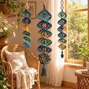 May include: Three hanging spiral ornaments crafted from crochet yarn in shades of blue, teal, and yellow. Each piece features intricate openwork patterns, suspended by rope with wooden rings, and accented with beads and a leaf-shaped charm.