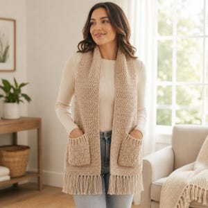 Può includere: Un gilet all'uncinetto color beige dal design lungo e aperto sul davanti, dotato di due tasche frontali con motivo a intreccio testurizzato e lunghe frange lungo l'orlo inferiore. Il capo è senza maniche ed è realizzato in filato.