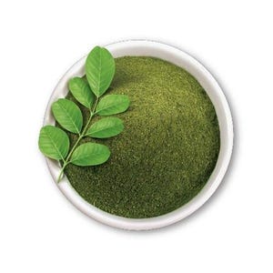 Peut inclure: Un bol blanc rempli d'une fine poudre vert foncé. Un petit rameau vert vif composé de plusieurs feuilles ovales est posé sur la poudre, contre le bord intérieur gauche du bol. La texture de la poudre est uniforme et finement moulue.
