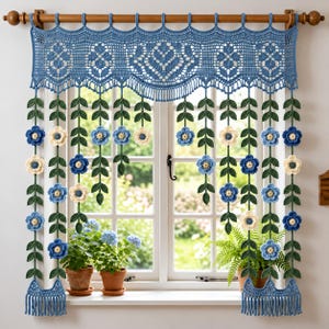 Puede incluir: Una cenefa de ventana tejida a ganchillo en azul con un intrincado patrón de encaje y tiras verticales colgantes. Cada tira muestra hojas tejidas en verde oscuro y flores tejidas en azul claro, azul oscuro y color crema.