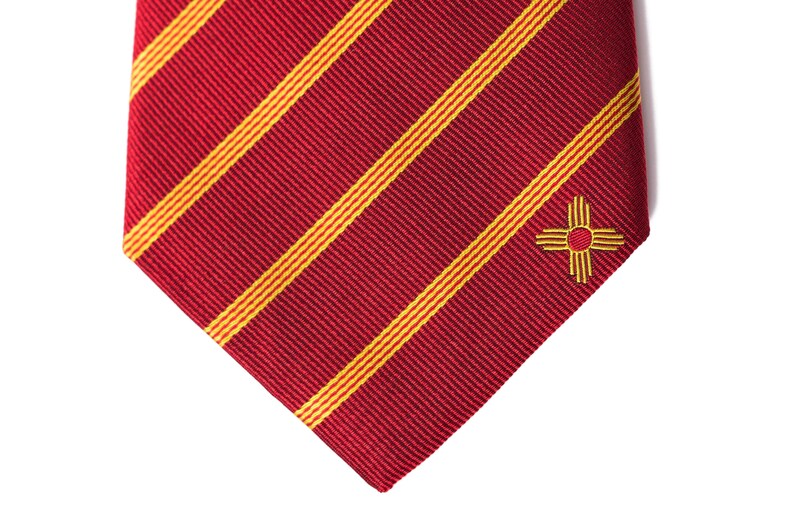 May include: Red and yellow striped tie with a small embroidered symbol of the state of New Mexico.
