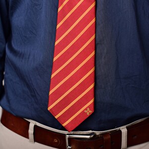 May include: A blue dress shirt with a red and yellow striped tie. The tie has a small gold emblem.