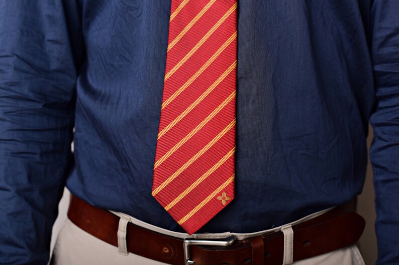 May include: A blue dress shirt with a red and yellow striped tie. The tie has a small gold emblem.