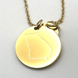 May include: A gold chain necklace with a round pendant featuring an outline of the state of Georgia.