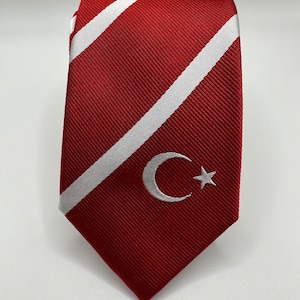 Op de afbeelding: Een rood-wit gestreepte stropdas met een wit halve maan en ster ontwerp.