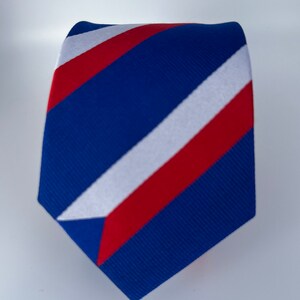 Op de afbeelding: Een blauwe, rode en witte gestreepte stropdas. De strepen zijn diagonaal en de stropdas is gemaakt van een textuur.