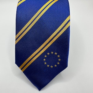 Op de afbeelding: Een blauwe zijden stropdas met twee gele strepen en een gouden cirkel van sterren in het midden.