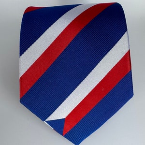 Op de afbeelding: Een blauwe, rode en witte gestreepte stropdas. De strepen zijn diagonaal en de stropdas is gemaakt van zijdeachtig materiaal.