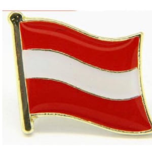May include: A gold-colored pin with a red and white Austrian flag design. The flag is waving in the wind.