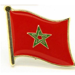 May include: A gold-colored metal pin with a red flag featuring a green five-pointed star. The star has a green outline and is centered on the flag.