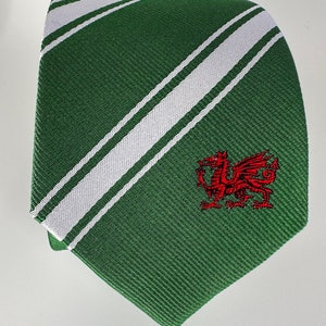 Op de afbeelding: Een groene stropdas met witte diagonale strepen en een geborduurde rode draak aan de voorkant.