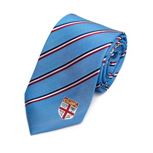 May include: A blue and white striped tie with a red stripe and a small embroidered crest in the center. The crest features a shield with a cross and other symbols.