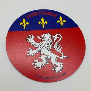 May include: A red and blue circular sticker with the text "LYON FRANCE" and three yellow fleurs-de-lis. A white lion with a red tongue is in the center of the sticker. The text "STATESMANTIES.COM" is at the bottom of the sticker.