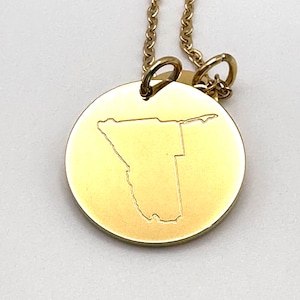 May include: Gold necklace with a round pendant featuring an engraved outline of the country of Namibia.