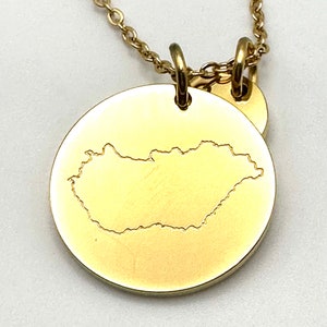 May include: Gold necklace with a round pendant featuring an outline of the country of Slovakia. The pendant is attached to a delicate gold chain.