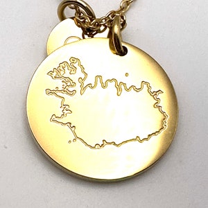 May include: Gold necklace with a round pendant featuring an outline of the country of Iceland.