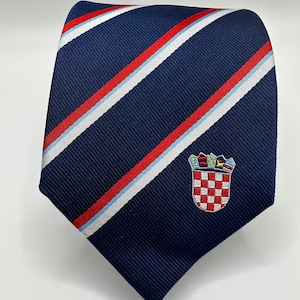 Op de afbeelding: Een donkerblauwe stropdas met rode en witte diagonale strepen en een geborduurd Kroatisch wapenschild op de voorkant.