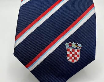 Może przedstawiać: Krawat w kolorze granatowym w czerwono-białe pasy ukośne z haftowanym herbem Chorwacji z przodu.