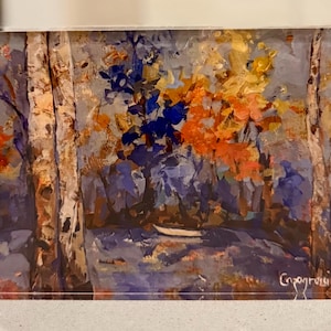 May include: An acrylic painting of a forest scene with birch trees, blue, orange, and yellow foliage, and a small boat on a body of water. The artwork is displayed in a clear acrylic frame with silver hardware.