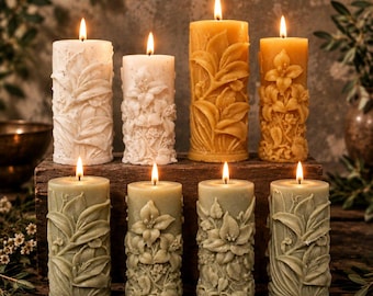 Pode incluir: Uma coleção de oito velas cilíndricas em branco, amarelo e verde sálvia, cada uma com padrões florais e de folhas em relevo. As velas estão acesas, com chamas visíveis, e dispostas sobre uma superfície de madeira escura.