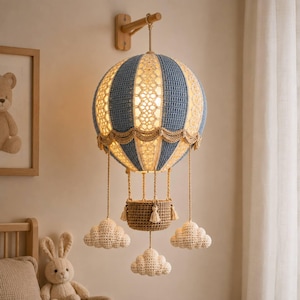 May include: A decorative hot air balloon lamp featuring a crocheted blue and cream striped canopy with intricate lace detailing. The balloon is suspended from a wooden wall mount and includes a small brown crocheted basket and three hanging clouds.