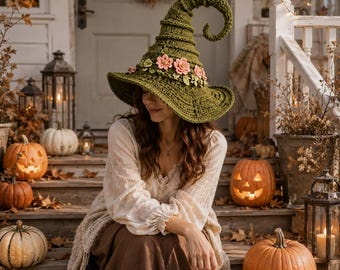 May include: A pointed olive green crochet witch hat featuring a curled tip and a decorative band of small pink and light green fabric flowers around the base. The hat has a wide, textured brim and is crafted with a detailed, ribbed stitch pattern.