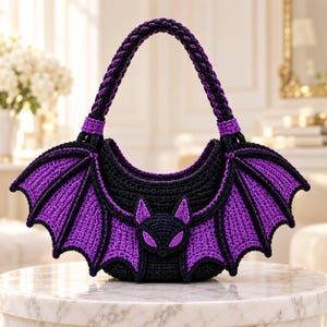 May include: A crescent-shaped crochet handbag featuring a black and purple bat design. The bag has a braided handle, a central bat face motif, and large, detailed bat wings extending from the sides, all crafted with black and purple yarn.