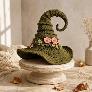 May include: A dark olive green crocheted hat with a tall, curved, pointed crown and a wide brim. The hat is decorated with a band of small, light pink crocheted flowers and green leaves encircling the base of the crown, featuring intricate textures.