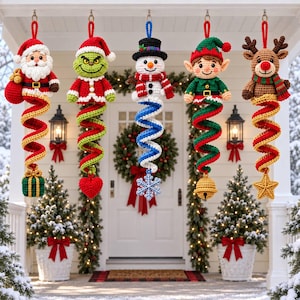 May include: Five crocheted Christmas ornaments hanging in a row, featuring Santa Claus, a green creature, a snowman, an elf, and a reindeer. Each figure is attached to a long, colourful spiral tail ending in a unique festive charm like a gift or star.