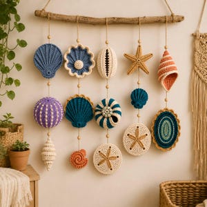 May include: A wall hanging featuring five vertical strands of crocheted marine life ornaments suspended from a horizontal driftwood branch. The ornaments include various shells, starfish, and sea urchins in shades of blue, purple, orange, and cream.