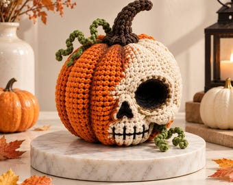 May include: A crochet pumpkin with a split design, featuring a bright orange side and a cream-coloured skull side. The pumpkin has a dark brown stem and curly green vines. The skull side includes a dark eye socket, nose, and stitched mouth.