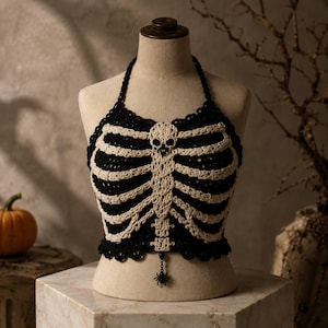 May include: A black crochet halter top featuring an off-white skeleton rib cage design on the front. The garment includes a skull detail at the neckline and a small black spider charm hanging from the bottom center hem on a thin chain.