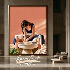 May include: A framed wall art print depicting a person with long dark hair wearing a navy blue tank top and a white apron, sitting at a pottery wheel and shaping a white clay bowl. The background is a solid peach color with soft light and shadows.