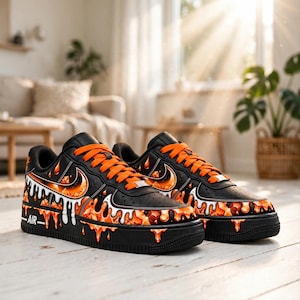 Könnte beinhalten: Ein Paar schwarze Sneaker mit leuchtend orangefarbenen Schnürsenkeln und einem Grafikdesign aus orangefarbener Flüssigkeit, die an den Seiten herabläuft. Die Schuhe haben eine schwarze Sohle, ein schwarzes Obermaterial und das Wort AIR in weiß.