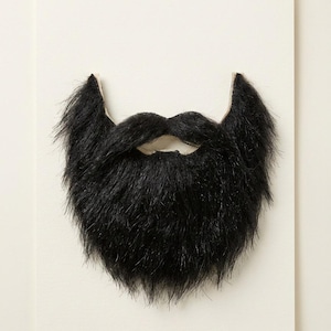 May include: A full, thick, black faux fur beard with a mustache. The facial hair accessory features long, textured synthetic fibers that create a voluminous appearance, designed to cover the chin and upper lip area with a realistic, dark aesthetic.