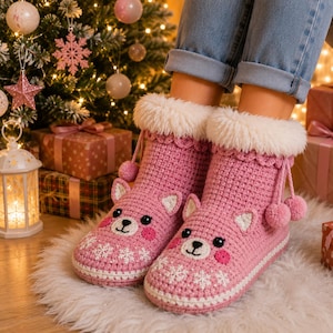 Peut inclure: Une paire de bottines en crochet rose avec un revers en fausse fourrure blanche, des liens à pompons et un motif de visage d'ours sur le devant. Les bottines sont ornées de flocons de neige blancs et possèdent des yeux noirs et des joues roses.